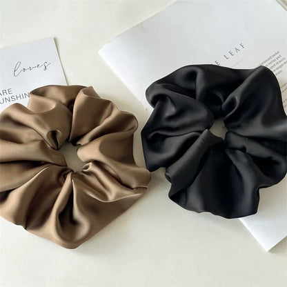 Lucia SCRUNCHIE XL two oversized satin scrunchies side by side in olive taupe and black, on magazine pages.