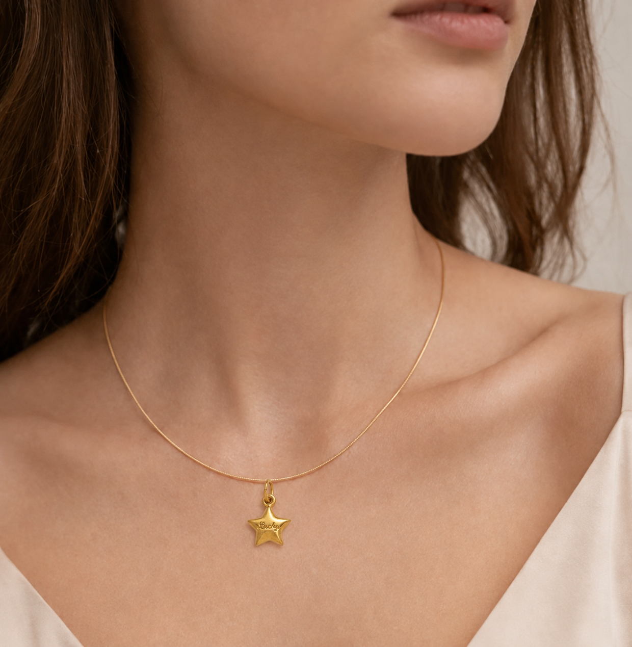 The Lucky Star CHARM worn as a pendant on a fine gold snake chain necklace, resting close to the neckline.