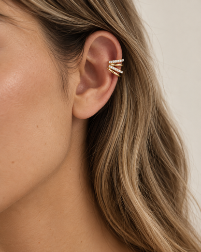 Gold triple-row pavé ear cuff worn close on a model's ear beneath a loose bun — Folie à Trois Lumen EAR CUFF.