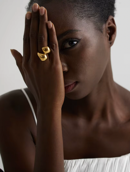 Model covers half her face with a hand wearing the gold Lunaire RING's two overlapping domes.