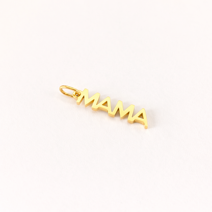 The Mama CHARM in a close-up flat lay, a gold vertical script pendant reading MAMA shown at an angle on cream fabric.