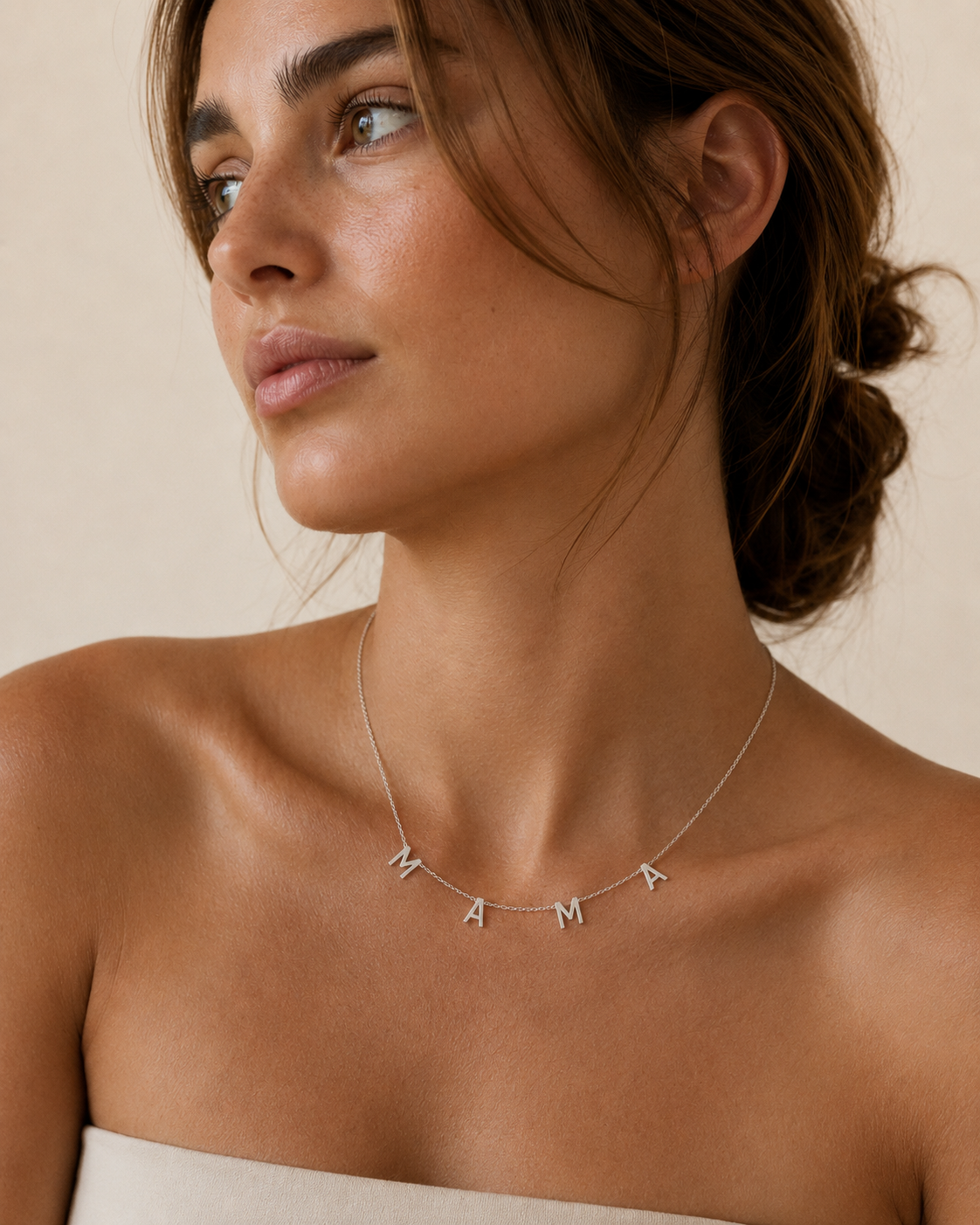 The Mama NECKLACE in silver worn at the neckline, individual letters spelling MAMA above a strapless top.