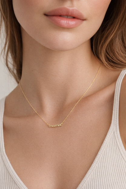 The Mama Small NECKLACE in gold worn at the neckline, the script mama pendant resting above a cream ribbed tank top.