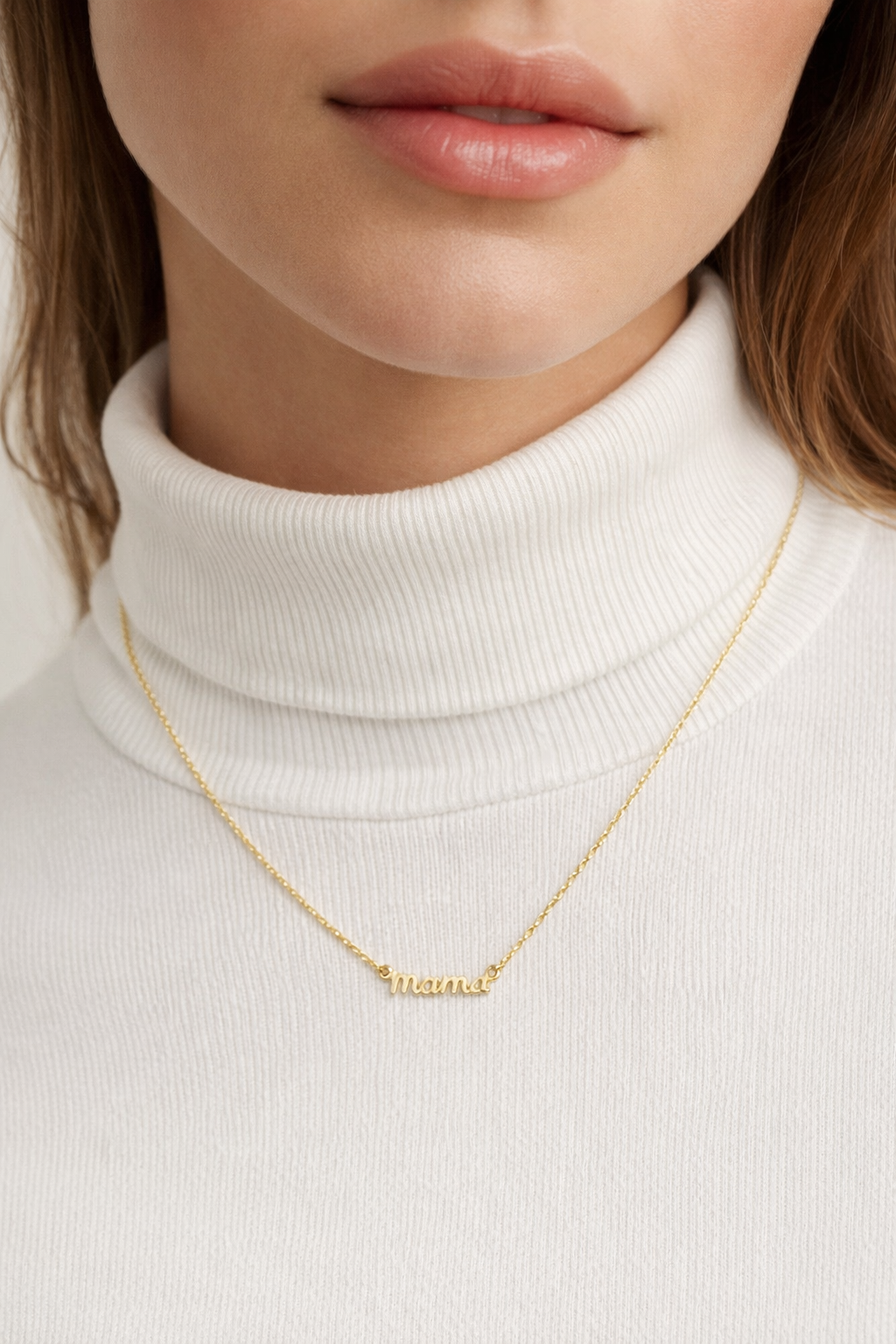 The Mama Small NECKLACE in gold worn at the neckline, the script mama pendant layered over a cream turtleneck sweater.