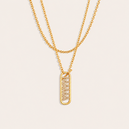 Layered gold chains with a pave mama tag pendant from the Mama Zircon Tag NECKLACE design, laid flat on beige.