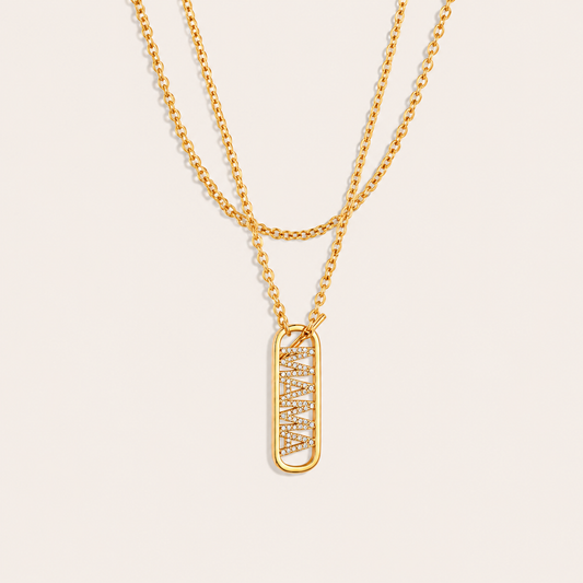 Layered gold chains with a pave mama tag pendant from the Mama Zircon Tag NECKLACE design, laid flat on beige.