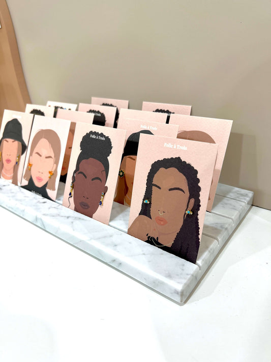 Marble tray with ridged slots holding illustrated Folie à Trois face cards with hoop and stud earrings on display.