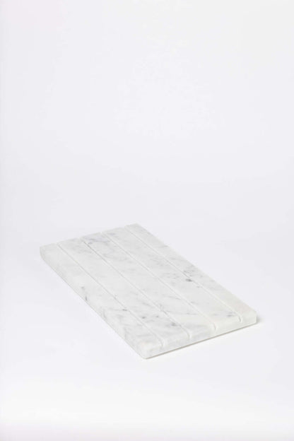 Single white marble tray with ridged slots for rings and earrings, angled against a plain white studio background.