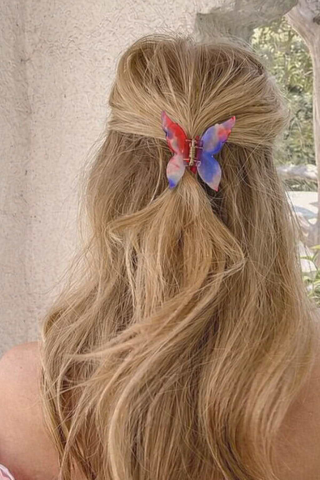 Mariposa HAIR CLIP's red, blue and white butterfly clip worn in half-up blonde hair against a stone wall.