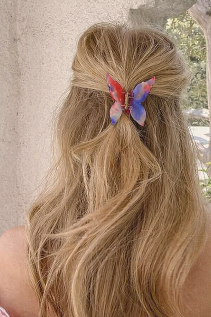 Mariposa HAIR CLIP's red, blue and white butterfly clip worn in half-up blonde hair against a stone wall.