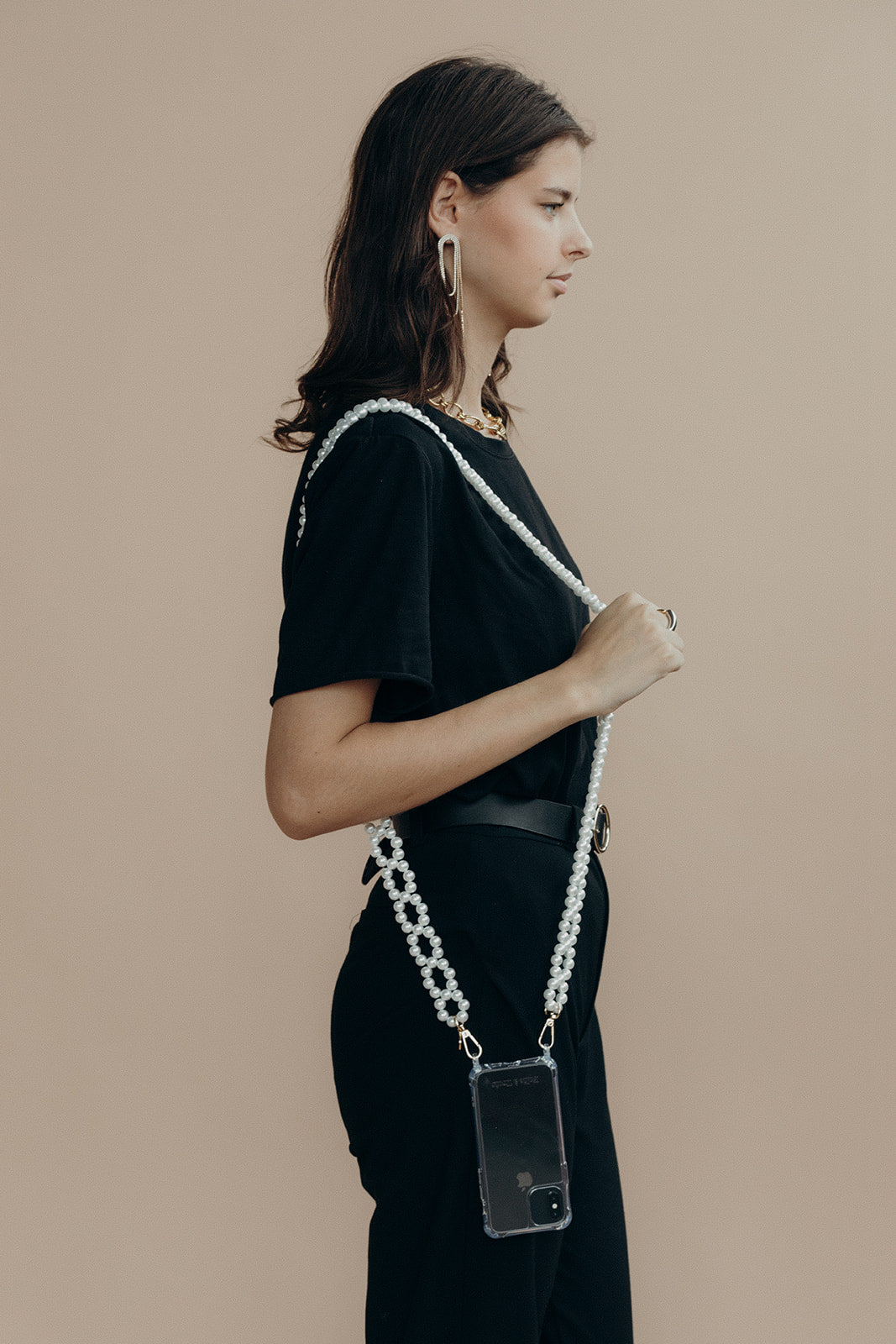 Side profile of a model wearing the Folie à Trois Marnie Pearl wholesale phone chain crossbody over a black t-shirt, phone in a clear case.
