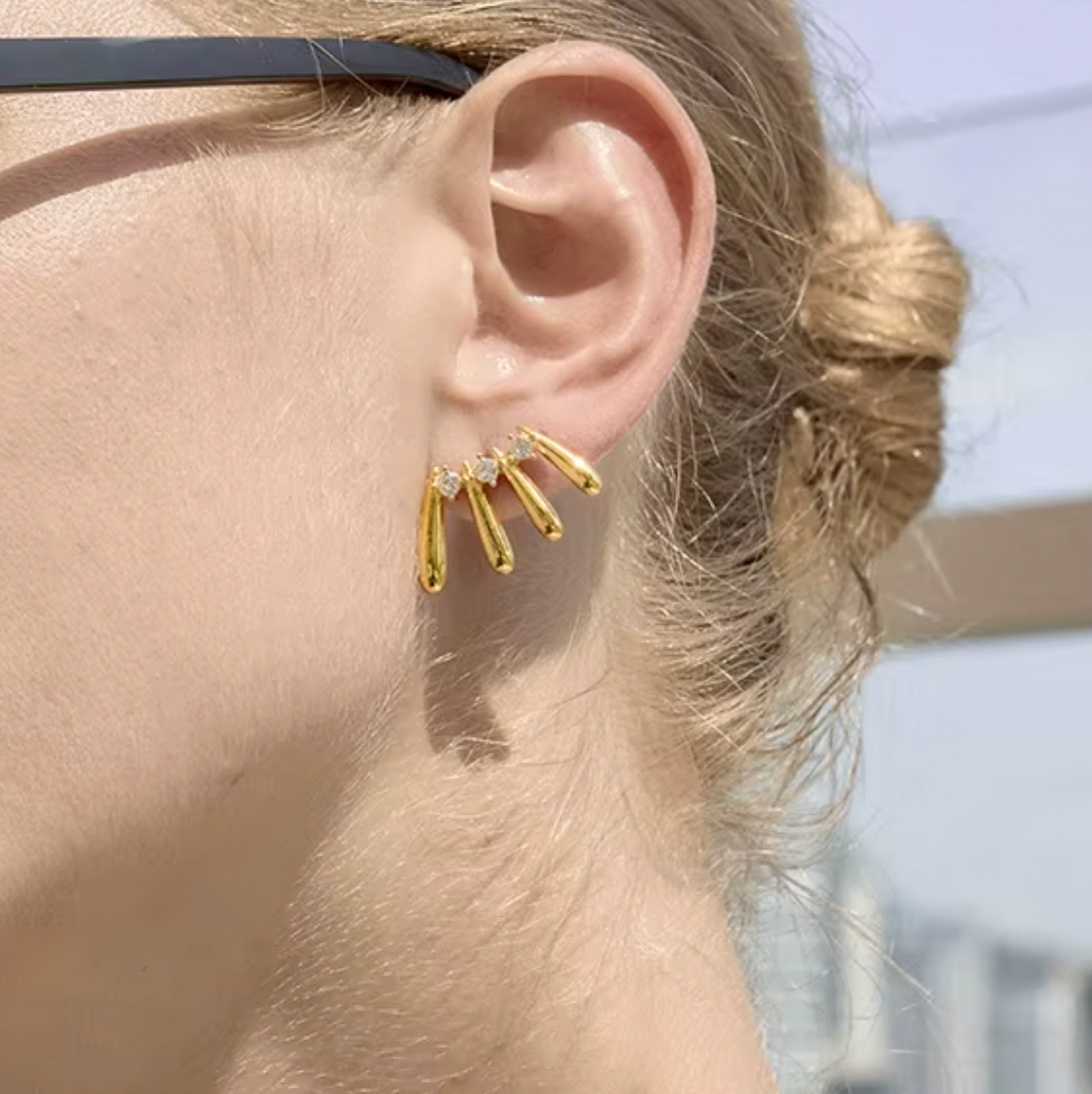 A model wears a gold Martina EARRINGS stud with four fanned teardrop bars and round cubic zirconia stones on her ear.