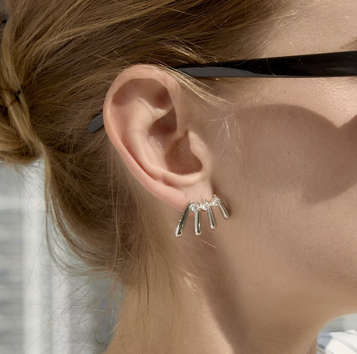 A model wears a silver Martina EARRINGS stud with four fanned teardrop bars and round cubic zirconia stones on her ear.