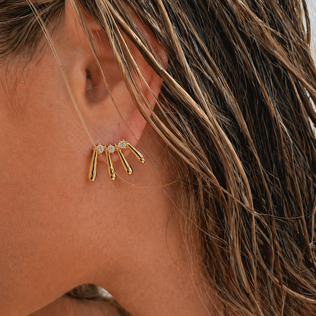 Close-up of a model wearing a gold Martina EARRINGS stud with four fanned teardrop bars and round cubic zirconia stones.