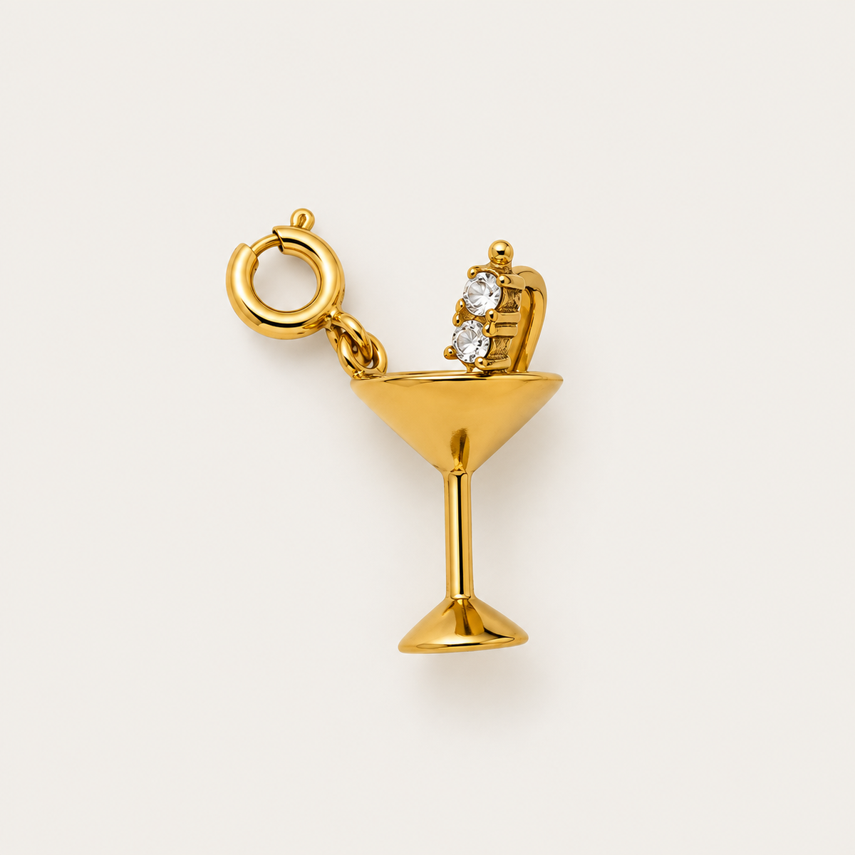 The gold Martini Glass CHARM with a two-zircon olive pick and spring ring clasp, shown in close-up on a cream background.
