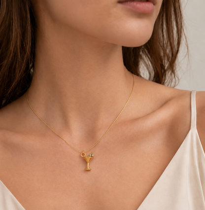 The gold Martini Glass CHARM worn as a pendant on a fine gold chain at the neckline of a model in an ivory satin camisole.