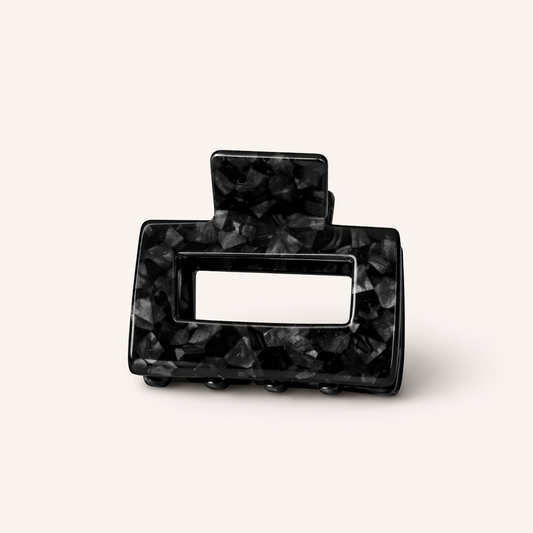 Black and charcoal marbled rectangular acetate claw clip with a cutout handle from the Mathilda HAIR CLIP collection, on a cream studio background.