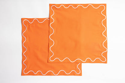 Two folded orange Maude napkins with white wave-trim edging, stacked flat on a white background.
