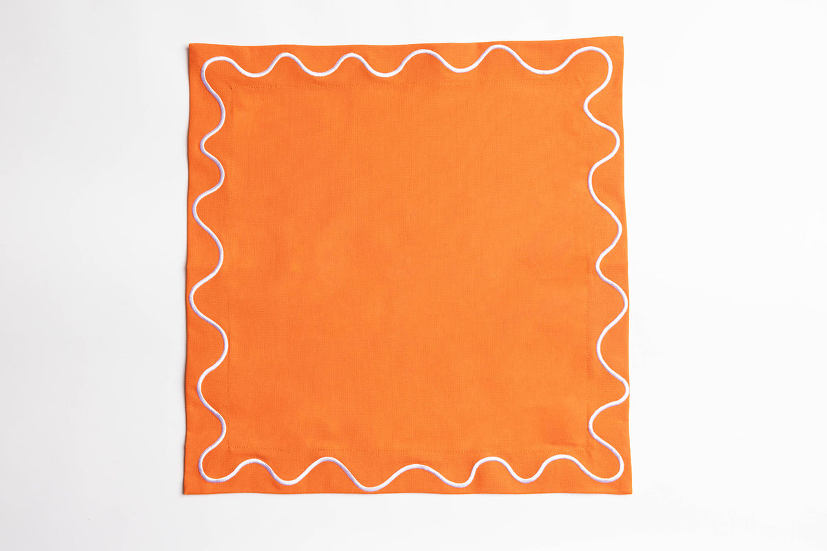 Single orange Maude napkin with a white wave-trim border, laid flat and square on a white background.