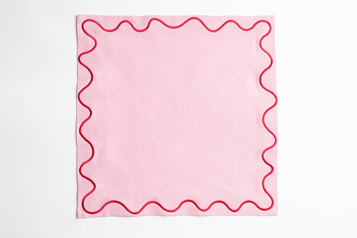 Single pink Maude napkin with a red wave-trim border, laid flat and square on a white background.
