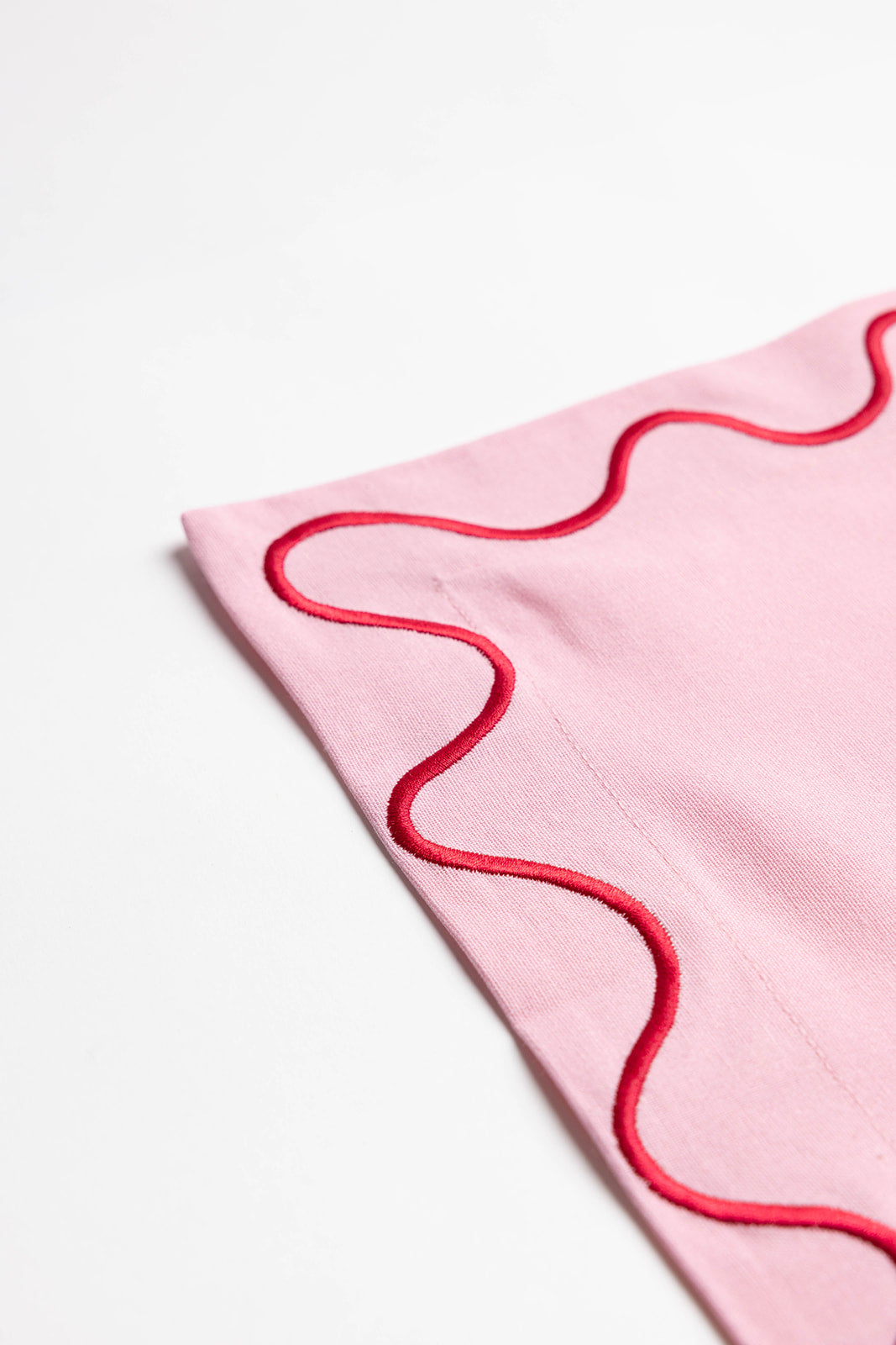 Olive-green Maude napkin edged with a cream scalloped wave-trim border, laid flat on a white surface.