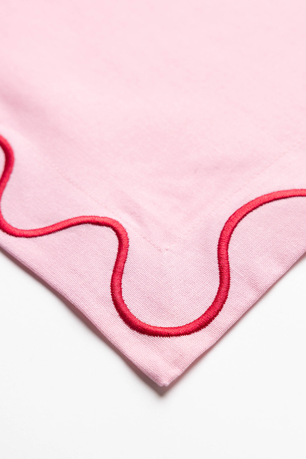 Close-up corner detail of an olive-green Maude napkin showing its cream scalloped wave-trim embroidery stitching.