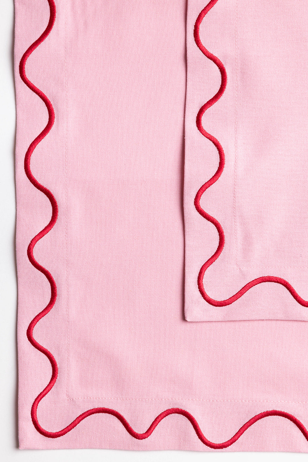 Red Maude napkin with a white wave-trim border and a delicate tied bow, laid flat on a light surface.