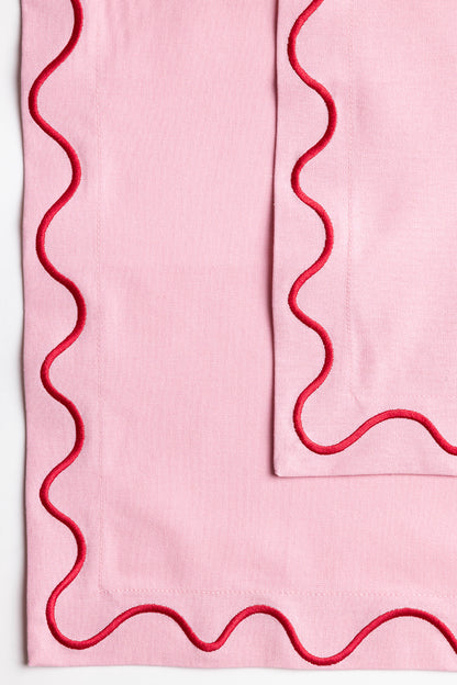 Red Maude napkin with a white wave-trim border and a delicate tied bow, laid flat on a light surface.