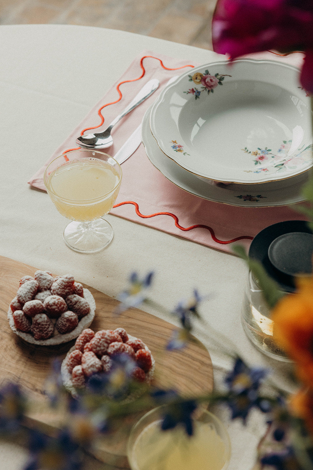 Styled table setting with a pink Maude napkin edged in orange wave trim, vintage floral plates and berry tarts.