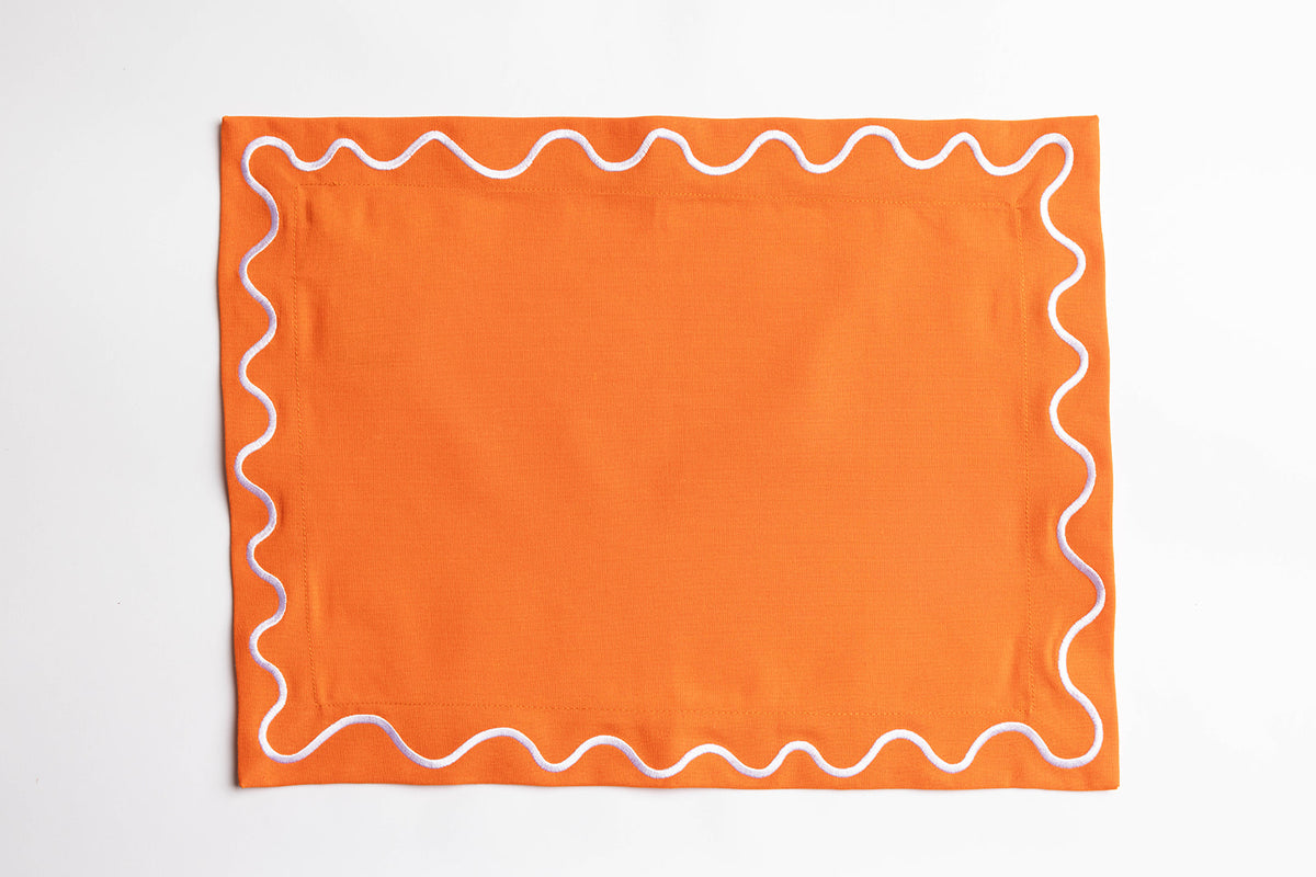 Orange Maude placemat edged with a white and lilac wave-trim border, shown flat against a plain white background.