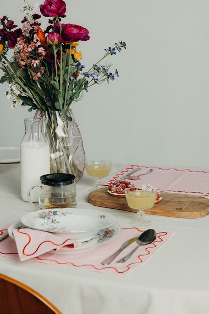 Khaki Maude wave-trim placemat set with white stacked plates, a coffee cup, fresh artichokes and lemons on linen.
