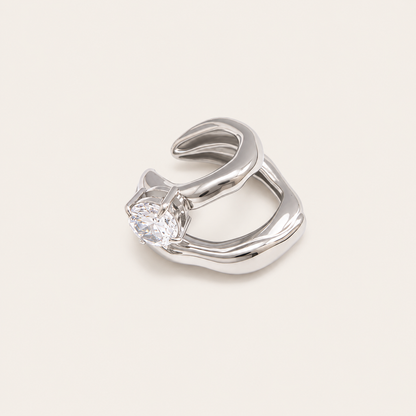 The Maya EAR CUFF in silver, a sculptural double-band cuff set with a single round clear gem, shown in a studio close-up.