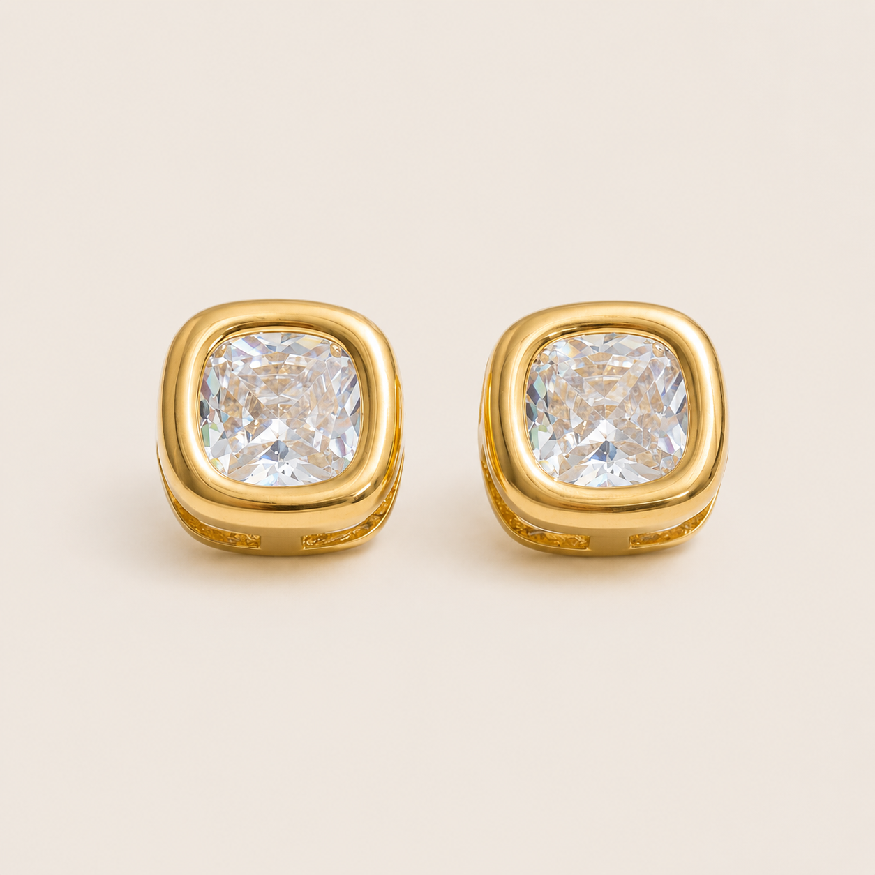 Gold stud earrings with a large cushion-cut white zirconia in a bezel setting on a cream backdrop — Folie à Trois Meridian EARRINGS