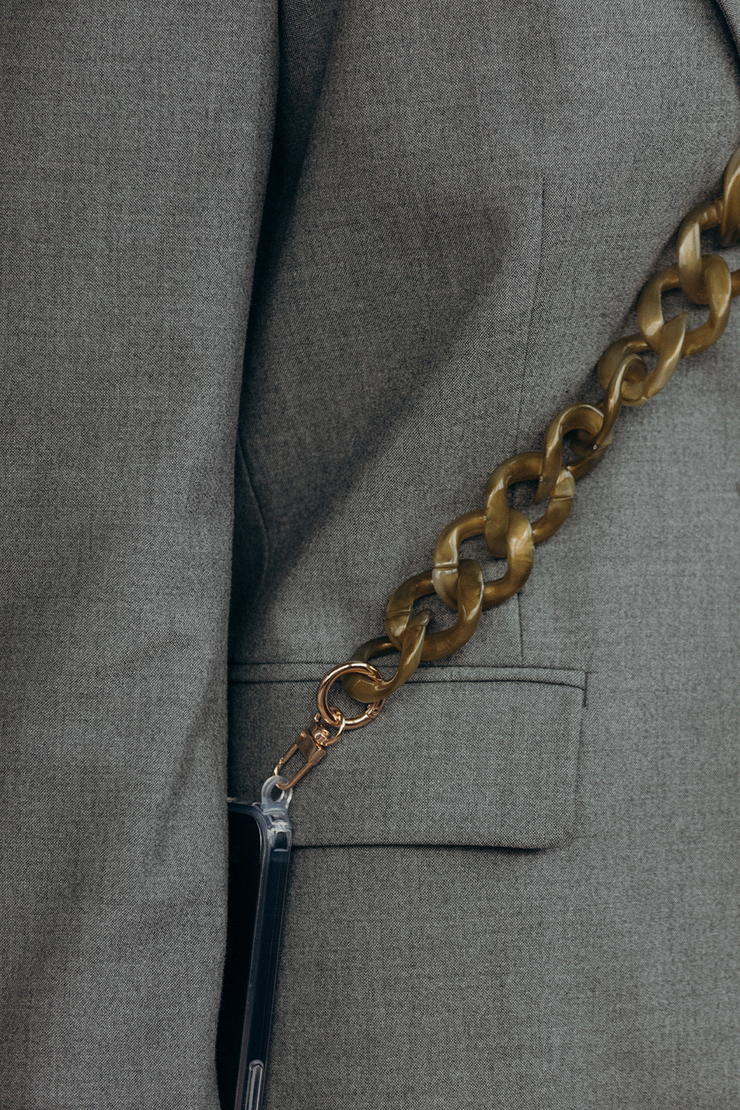 Close-up of a bronze marbled curb-link phone chain attached to a phone case, resting against a grey blazer pocket.
