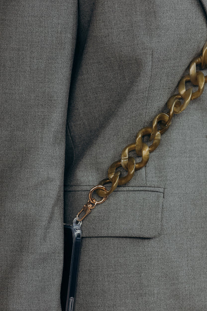 Close-up of a bronze marbled curb-link phone chain attached to a phone case, resting against a grey blazer pocket.