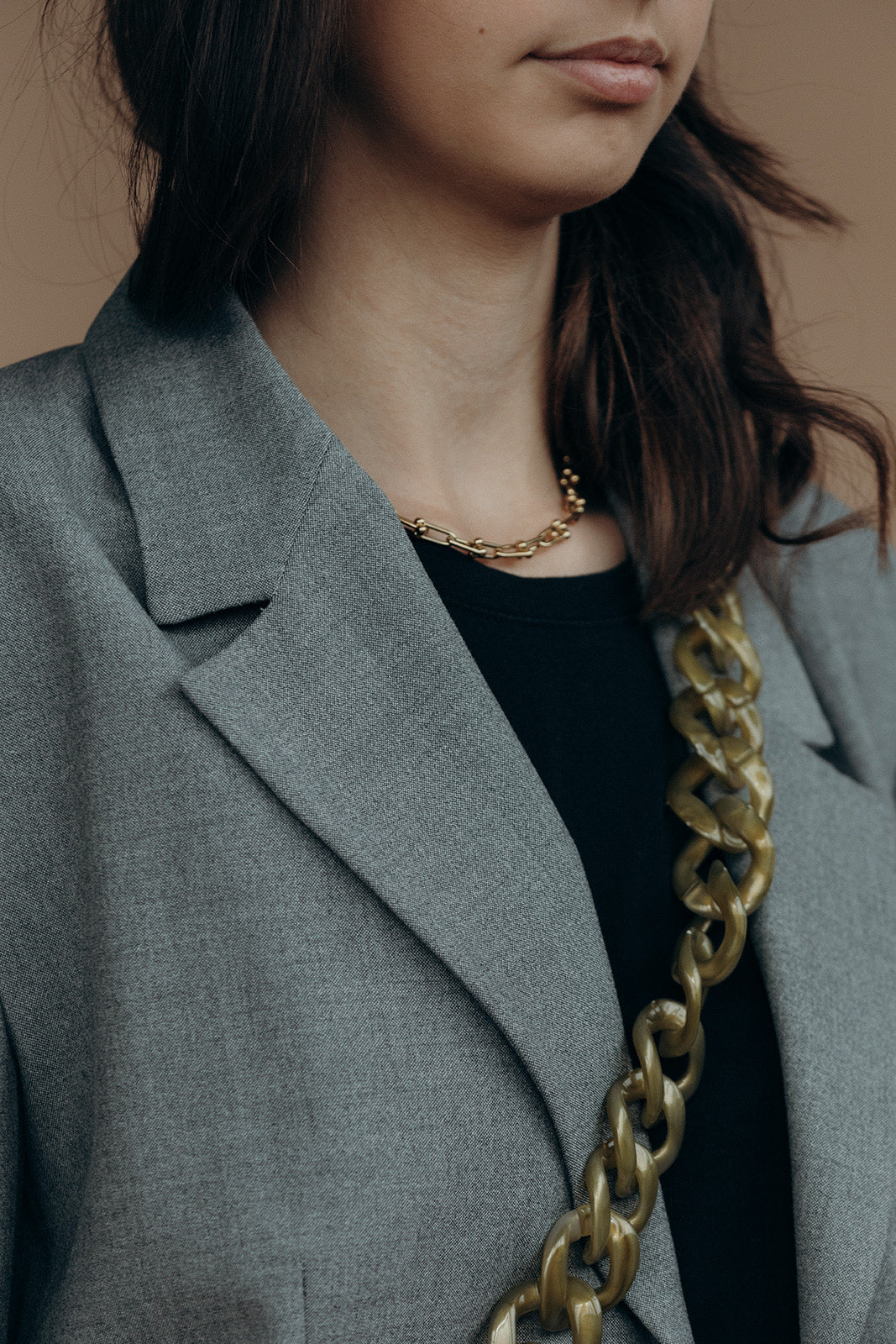 Close-up of a bronze marbled curb-link phone chain draped over the shoulder of a grey blazer, near a gold necklace.