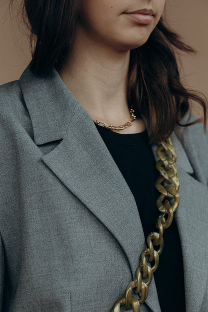 Close-up of a bronze marbled curb-link phone chain draped over the shoulder of a grey blazer, near a gold necklace.