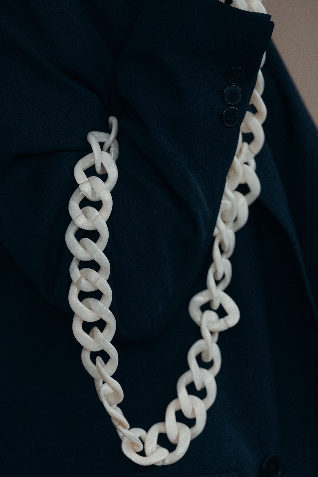 A white acrylic curb-link phone chain with gold clasps, draped over the sleeve of a navy blazer.
