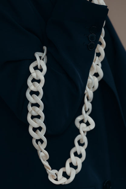 A white acrylic curb-link phone chain with gold clasps, draped over the sleeve of a navy blazer.