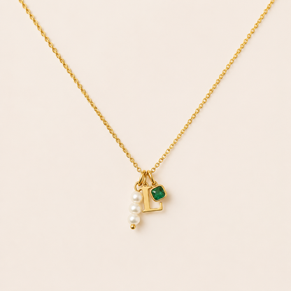 The Minimal NECKLACE in close-up, a gold L initial charm, cluster of pearl beads, and a square emerald charm on a fine chain.