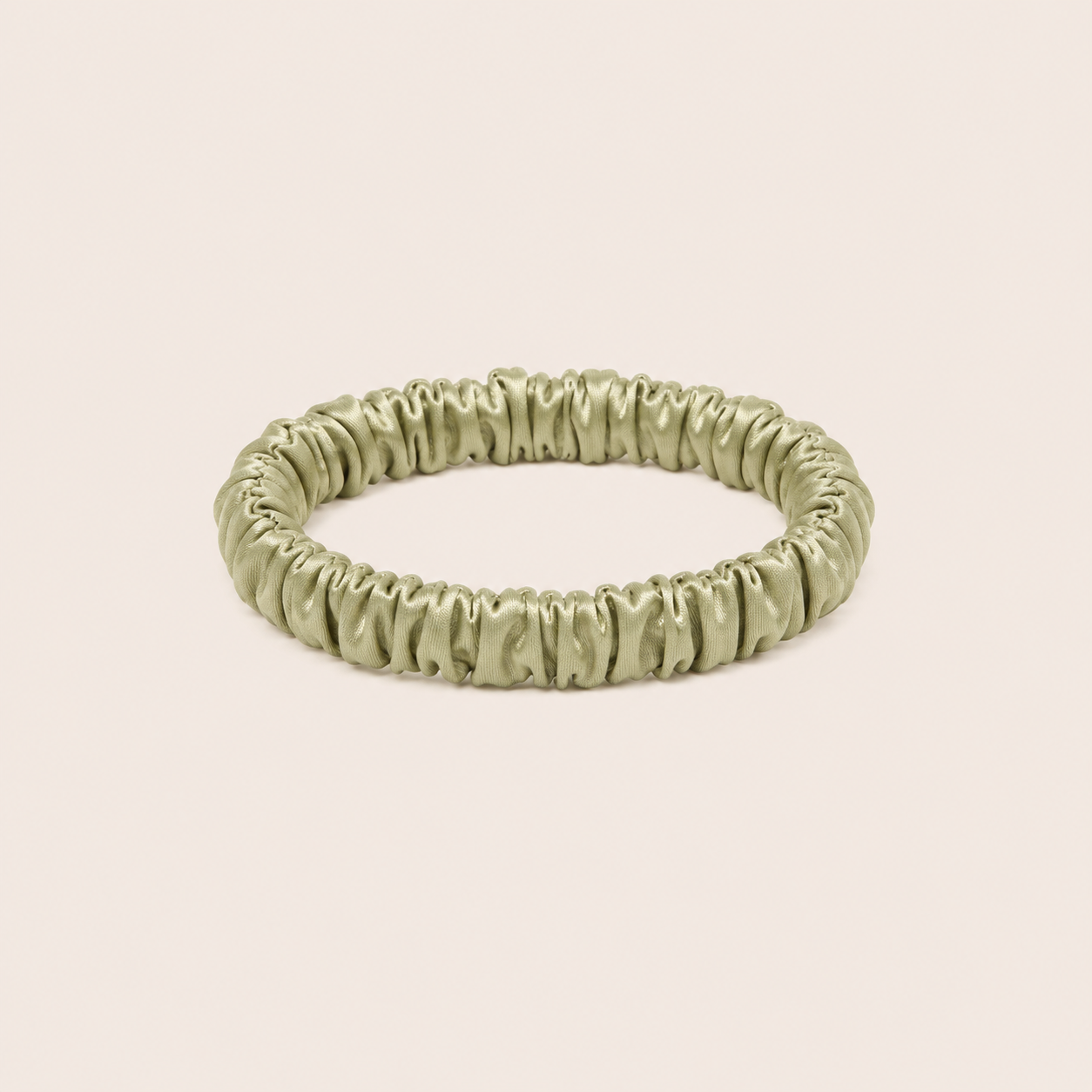 Minnie SCRUNCHIE S small satin scrunchie in sage green, studio shot on a solid pale pink background.