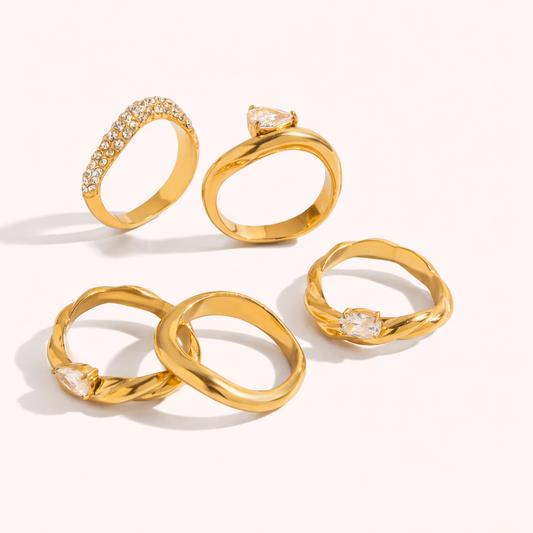 Flatlay of five gold Misbehave RING styles together, including a pavé band, a twisted rope band and wavy bands with clear stones.