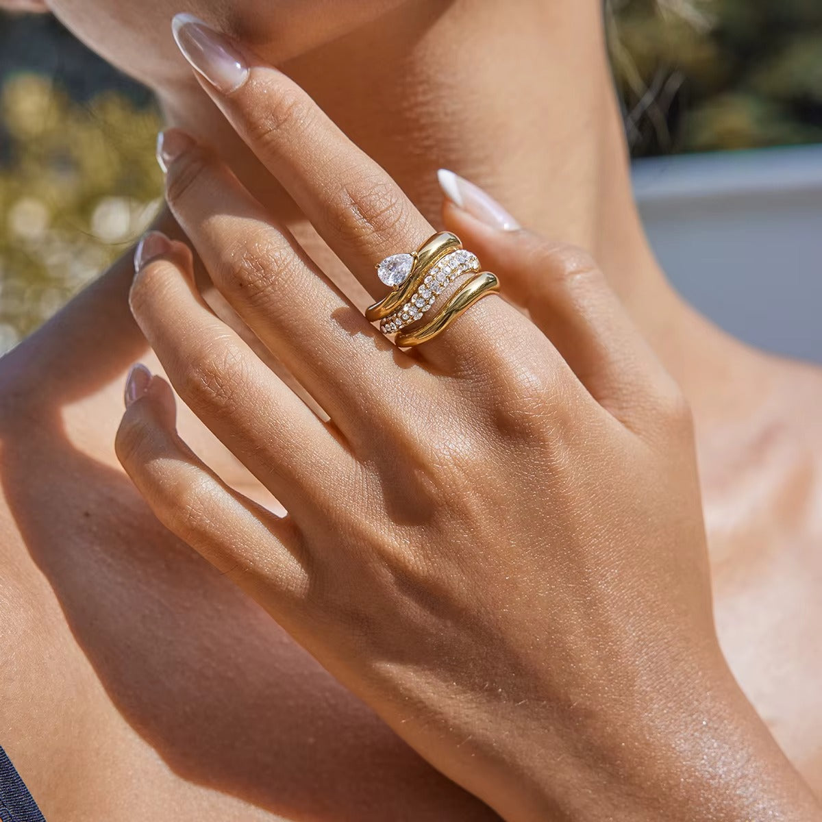 Close-up of a hand near the neck wearing a stacked pair of gold Misbehave rings, a pear-stone band paired with a pavé wave band.
