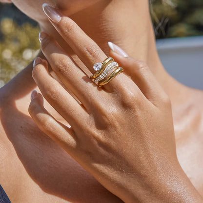 Close-up of a hand near the neck wearing a stacked pair of gold Misbehave rings, a pear-stone band paired with a pavé wave band.