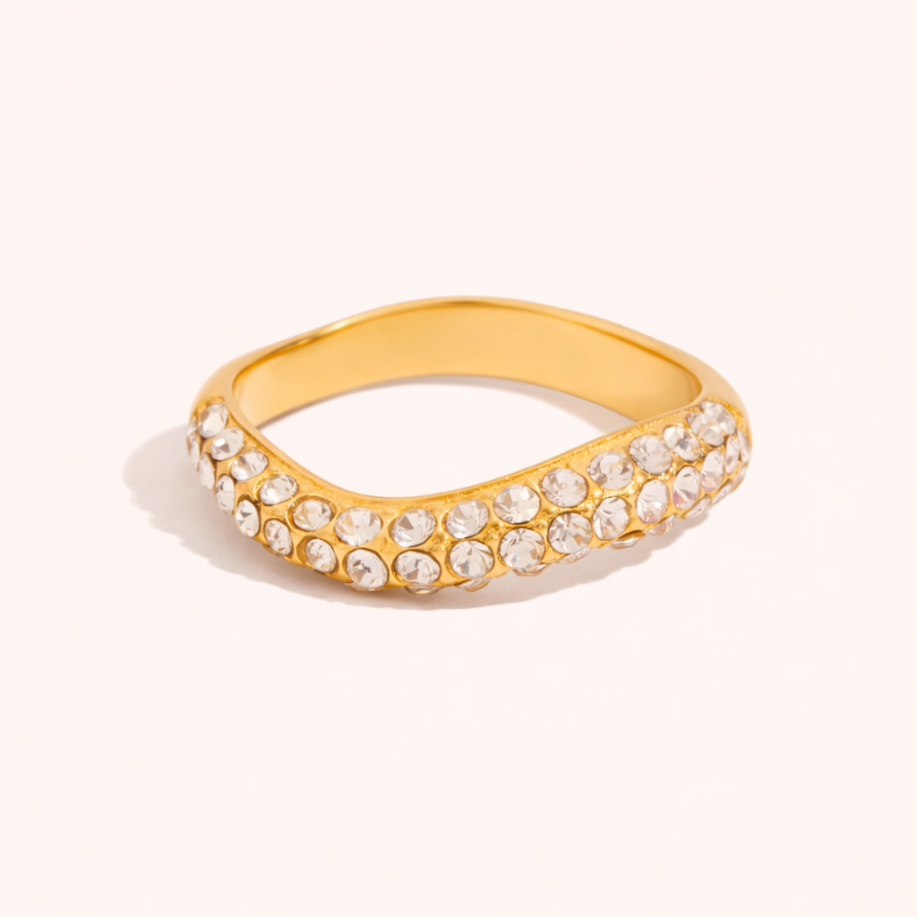 Wavy gold Misbehave RING fully paved with small clear stones along the band, shown on a cream backdrop in studio.