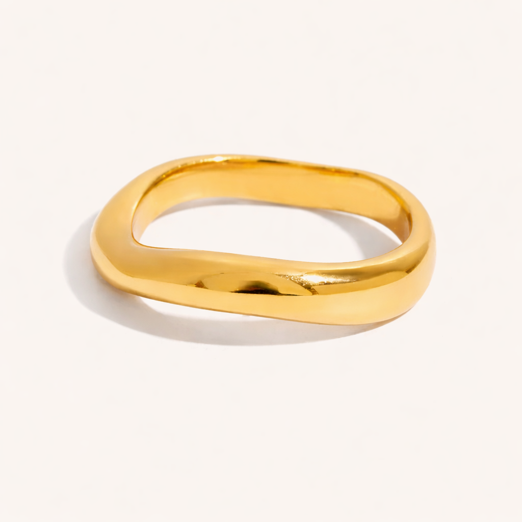 Plain smooth wavy gold Misbehave RING band with no stones, shown on a cream backdrop in studio.