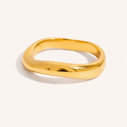 Plain smooth wavy gold Misbehave RING band with no stones, shown on a cream backdrop in studio.