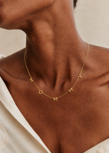 The Mommy NECKLACE in gold worn at the neckline, individual gold letters spelling MOMMY on a fine chain.