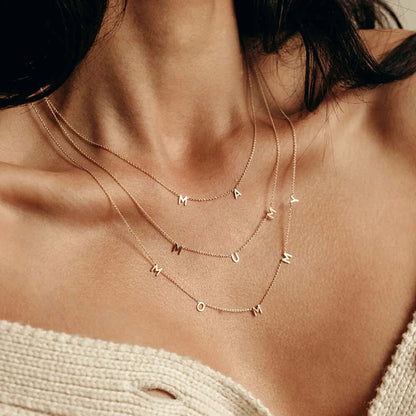 The Mommy NECKLACE layered with MAMA and MUM necklaces at the neckline, three fine gold chains with dangling letters.