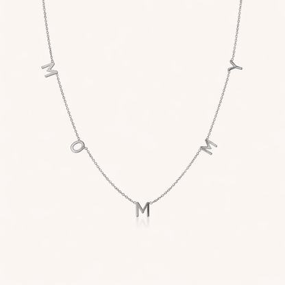 The Mommy NECKLACE in silver, individual letters spelling MOMMY dangling from a fine chain, shown on a cream background.